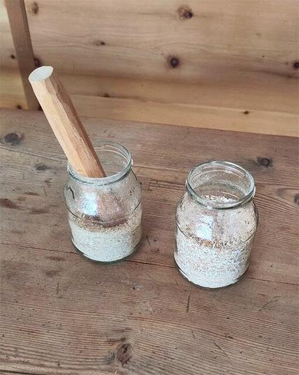 Crushedegg shells in two jars with a wooden pestle in the left one on a  larch wood table. Arrola pine boards panelling in the background.