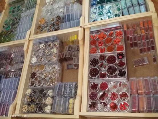 Photo de tiroirs en bois posés côte à côtes, remplis de boites transparentes pleines de perles, bien rangées pas couleurs.