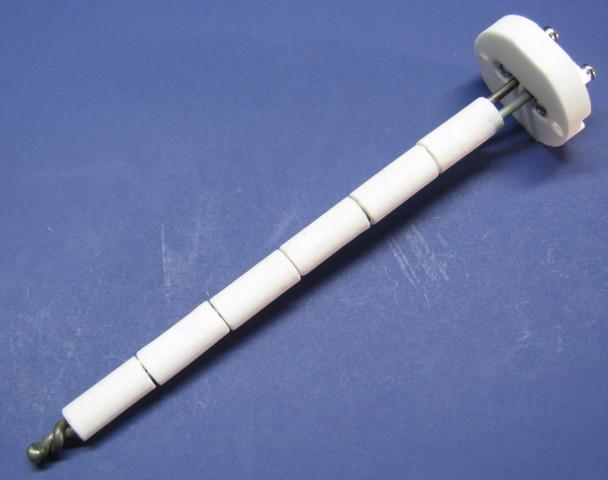 A photo of a white high temperature thermocouple on a blue surface. The sensor has a two prong wire that is twisted at the tip, and 6 white ceramic insulators. At the right top is a ceramic base plate with metal screw terminals that are used to connect a wire that will run to a digital thermometer. This sensor is used in pottery kilns