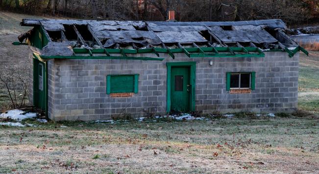 A rural abandoned building with green trim paint and a largely missing roof.