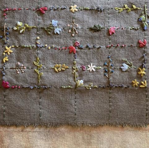 Flowers and leaves embroidered in a grid pattern on a piece of gray fabric.