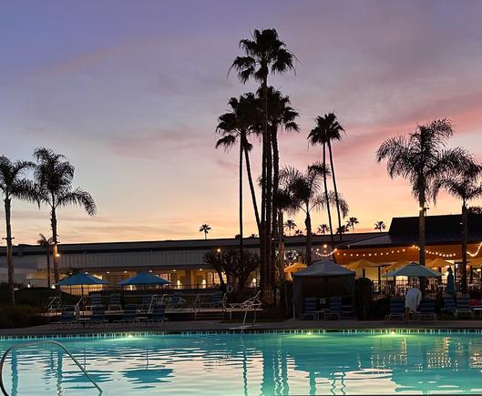 View of the hotel as lights come on after sunset. Reddish sky contrasts with almost fluorescent blue green color of the pool in the foreground reflecting the tall palm trees