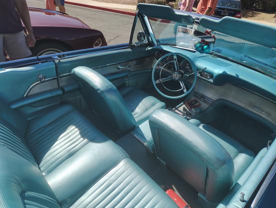 This photo looks into the interior of the 1961 Thunderbird convertible from the back.  As was the custom in cars of the era, the entire interior, including the steering wheel and the dashboard, match the light turquoise vinyl upholstery color.  The futuristic trim beneath the instrument panel is ridged brushed aluminum.  It extends all the way across in front of the passenger seat, and back down the center console.  Ford offered the swing away steering wheel for the first time in this car this year.  It is shown slid over to the right, to allow easier ingress and egress from the car.