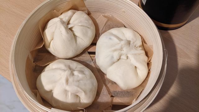 3 nikuman inside a bamboo steamer. It's like a small basket with a bamboo lid that can be placed on a steaming pot.