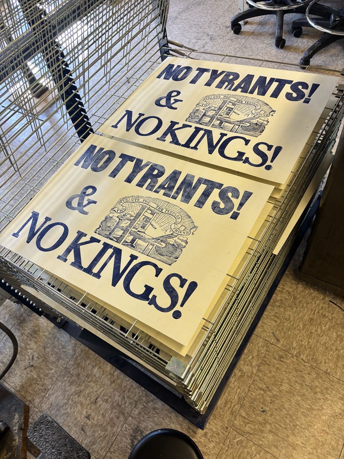 Two large posters on off white paper with blue ink reading:  NO TYRANTS! & NO KINGS!   In large wood type font. There is a large image cut of a wooden printing press with a banner of text above it reading “THE TYRANTS FOE THE PEOPLES FRIEND”