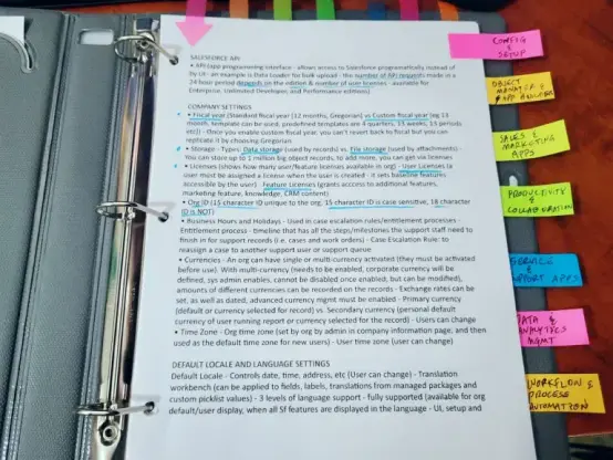 Inside of the physical (printed) Salesforce admin exam study guide I made, a binder with colored tabs, text, things highlighted, on a wood grain desk, in front of a keyboard
