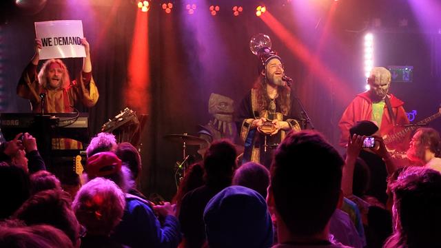 Die vierköpfige Band Henge im Kohi in Karlsruhe. Zwei der Bandmitglieder tragen Alienmasken, der Sänger trägt einen Hut mit einer Plasmakugel.