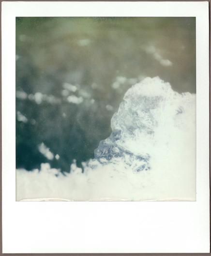 Close-up Polaroid of a bit of ice in the lower right, some of the crystals visible in focus, above blurry running water.