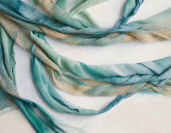 A twisted teal and beige abstract arrangement of strips of imaginary fabric remnants, a bit worn and aged, showcasing soft textures, flowing lines, and gentle folds against a clean white background.