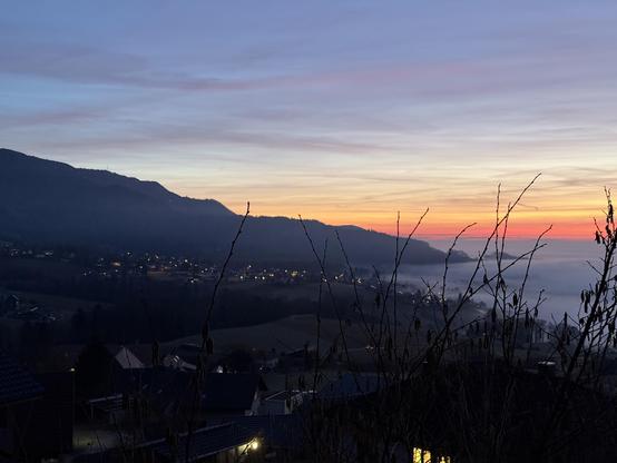 A view from our front window into the open. There's part of the nearby mountain. Clouds are creeping in slowly and the sun makes the horizon glow orange.