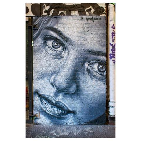 Colour photo of a street art painting of a girls face on a wall in the Leake Street Arches