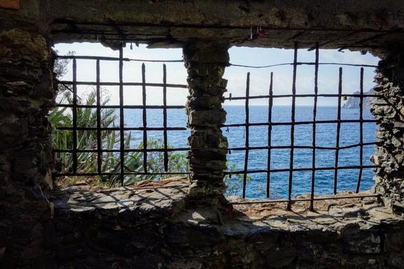 A two-paned window with a view of the ocean. The window is set in a stone wall and is covered with a rusty metal grid.
The window is rectangular, and the two panes are separated by a thick stone pillar. The stone wall surrounding the window is made of large, rough-hewn stones. The metal grid is made of thick, rusty bars that are spaced apart. The bars are twisted and bent in places, as if they have been damaged over time.
Through the bars of the grid, you can see the ocean. The water is a deep blue colour, and it is calm.
The ground in front of the window is covered in shadows.
Overall, the image is evocative of a place that is both beautiful and mysterious.
The ocean view is peaceful and inviting, but the rusty grid and the damaged stone wall suggest a history of neglect and decay.