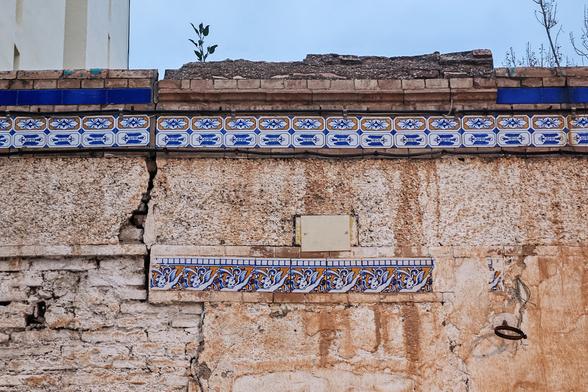 A weathered wall decorated with rows of ceramic tiles with patterns in blue and yellow