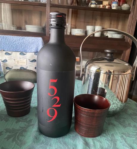 Photo of a black bottle of Shochu next to 2 small wooden glasses and an ice bucket.