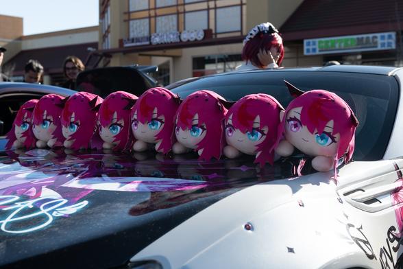 A row of plushies on the hood of a car with Anime wrap