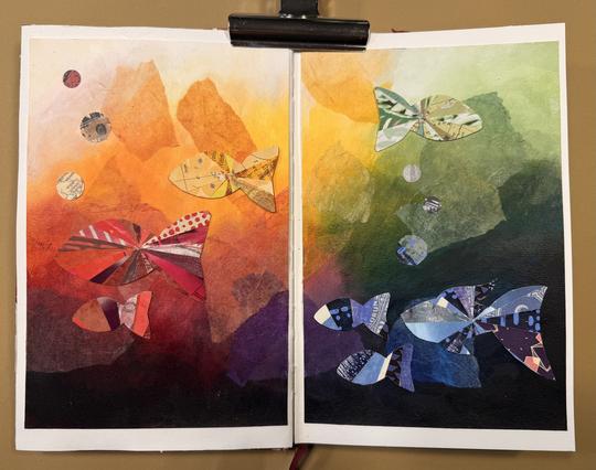 Das Bild zeigt ein abstraktes Kunstwerk mit einer Unterwasser-Szene, bestehend aus zwei nebeneinanderliegenden Seiten in einem Skizzenbuch. Der linke Bereich ist von warmen Farben wie Rot, Orange und Gelb dominiert, während die rechte Seite kühle Töne wie Grün, Blau und Schwarz aufweist. Collagierte Fische aus gemusterten Papierstücken schwimmen durch die Szene – rote und orangefarbene Fische auf der linken Seite, blaue und violette Fische auf der rechten. Blasen aus bedrucktem Papier steigen auf. Die Farbverläufe und die Transparenz der Papierschichten verleihen dem Werk Tiefe und Bewegung. Ein Clip hält das Art Journal oben offen.