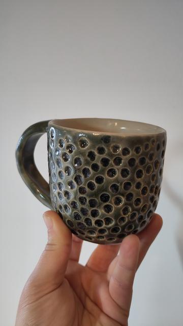 Una mà sosté una tassa verda amb textura de cercles.
