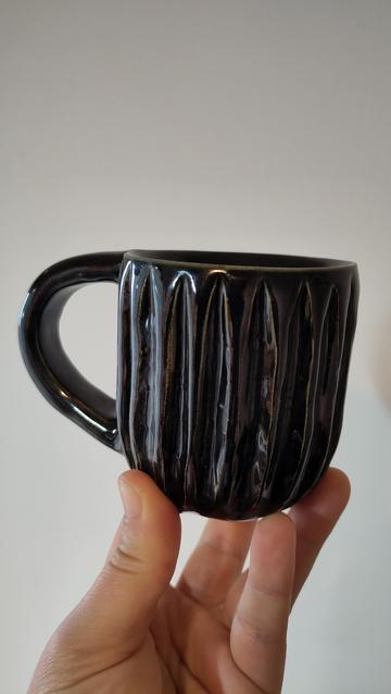 Una mà sosté una tassa de ceràmica fosca amb textura de ratlles verticals.