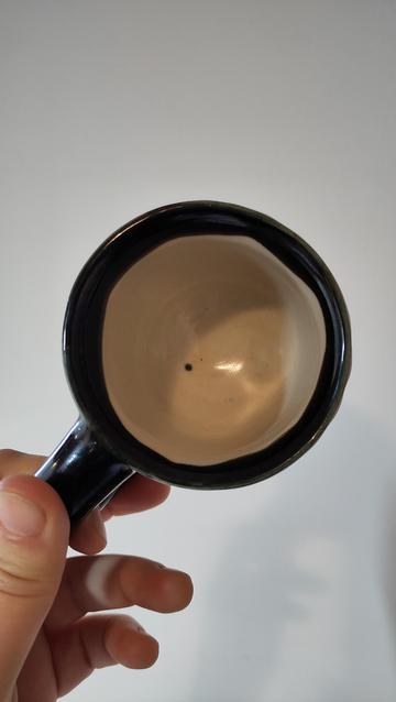 Una mà sosté la tassa negra, veiem l'interior, blanc amb un punt negre.