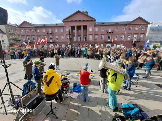 Blick vom Stadtkirchenportal in Richtung Rathaus. Man sieht die Band von hinten und die richtig große Demo-Crowd im Hintergrund. Viele Leute haben regenbogenfarbene Flaggen oder Demoschilder dabei.