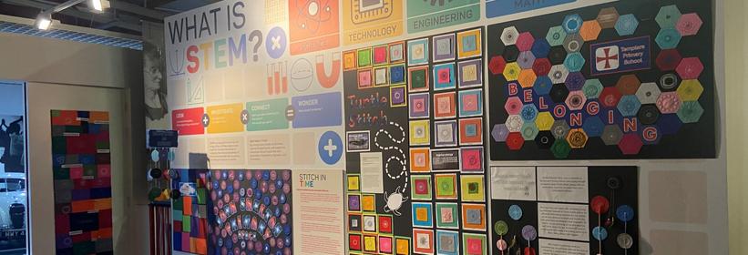 Photograph shows childrens work on display at Coventry Transport Museum. On the wall are collages of work done by primary school children. Each collage is made up of a collection of patterns stitched onto brightly coloured felt.