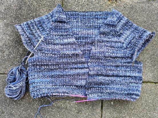 A handknit cardigan in progress. It's done from top down, with a v neck. It's now 17 cm below the point where the sleeves were split off and the sts put on separate needles, waiting to be finished. 

Yarn is in shades of blue and grey, creating an irregular stripey effect.