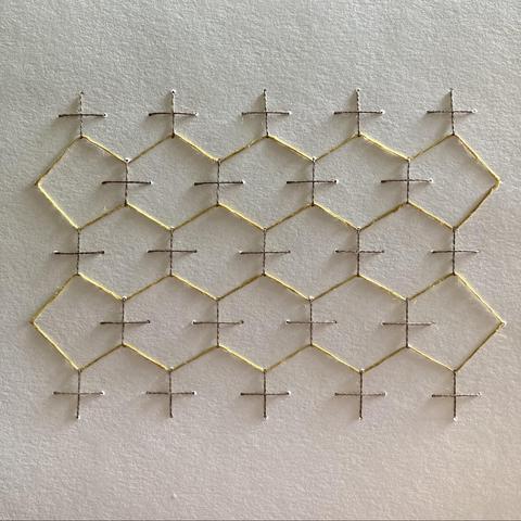 A honeycomb pattern in yellow linen thread stitched on white paper.