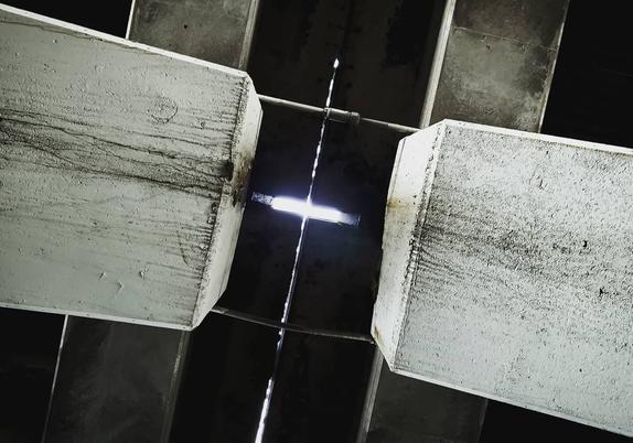 A black and white photo of the underside of interstate 95, featuring concrete support braces. Daylight can be seen through a gap in the road deck.
The framing of the high contrast photo is set at a slight angle.