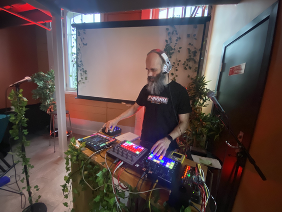 Electronic musician with headphones with his gear. Fake ivy decor.