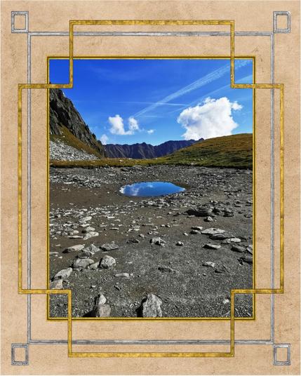 Un ciel bleu avec de rares nuages. En arrière plan, une barrière montagneuse à la pierre sombre. Des collines de verdures entourent un cercle rocailleux au centre duquel se trouve un petit point d'eau.