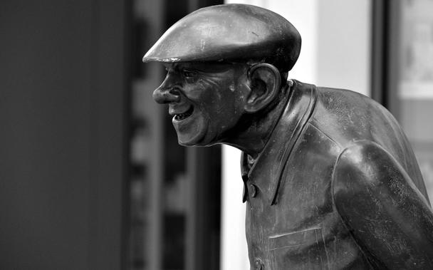 Bronze statue of a man wearing a hat, showcasing intricate details and a classic pose. 

Bronzestatue eines Mannes, der einen Hut traegt, mit aufwasendigen Details und einer klassischen Haltung.
