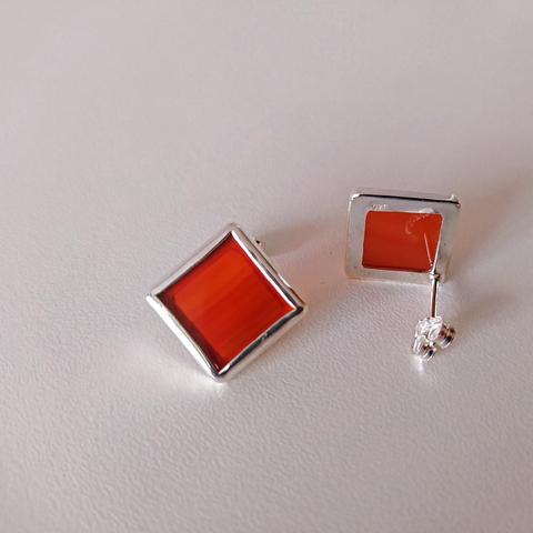 a pair of silver romboid stud earrings with red gemstone