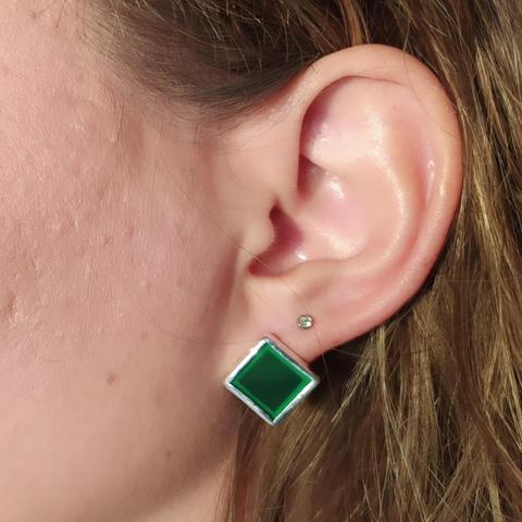 a green-silver romboid stud earring worn on ear