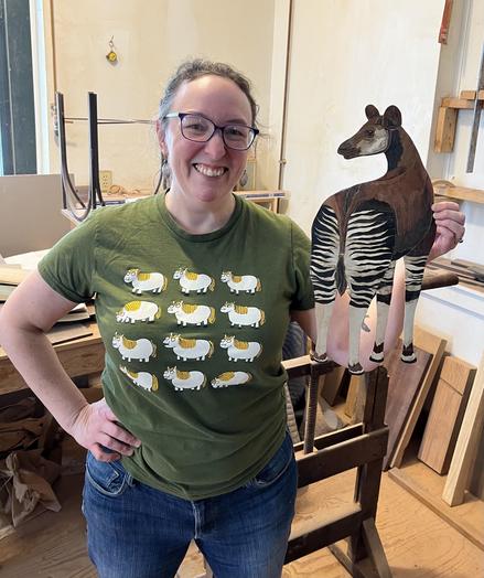 Photograph of me smiling and holding the cut-out okapi in the woodshop.
