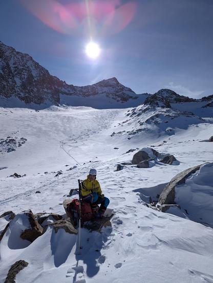 A skier taking rest on a rock with the lower part of the Sommerwandferner and ski tracks behind him.