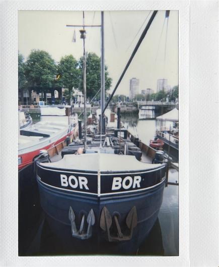 The front view of a big boat. It’s dark coloured. The name of the boat, Bor, is painted on in white lettering. Two anchors hang from the front.