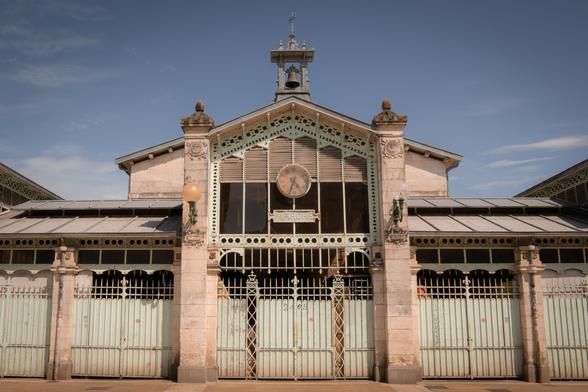 A historic market hall in La Rochelle, France, featuring ornate ironwork, pastel-colored gates, and a symmetrical façade. The building’s vintage charm, central clock, and soft lighting evoke a Wes Anderson aesthetic.