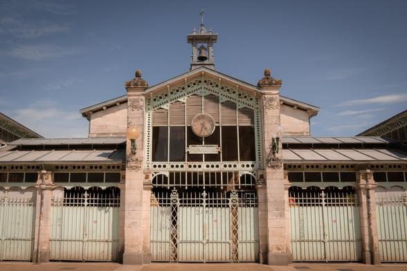 A historic market hall in La Rochelle, France, featuring ornate ironwork, pastel-colored gates, and a symmetrical façade. The building’s vintage charm, central clock, and soft lighting evoke a Wes Anderson aesthetic.