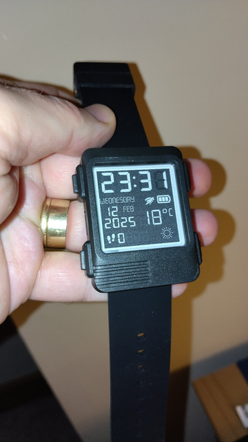 A chunky e-paper/e-ink watch with a black and white display, showing large LED style numbers, step count, wifi indicator, date, step count and weather forecast.