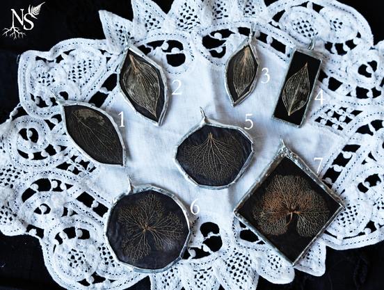 English 6 stained glass pendants showcasing skeleton leaves and petals on black backgrounds laying on a white crochet doily. Some pendants are rectangles, rounds, leaf-shaped… There are numbers next to each pendant.
❉
Français 6 pendentifs en vitrail mettant en valeur des feuilles et pétales dont il ne reste que les nervures sur fond noir posés sur un napperon au crochet blanc. Certains pendentifs sont des rectangles, d’autres des ronds, des formes de feuilles… Il y a des numéros à côté de chaque pendentif.
