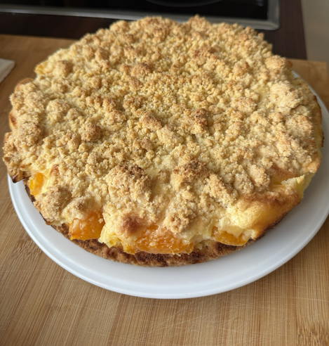 Auf einem weißen Teller liegt ein goldbrauner Streuselkuchen. Am Rand sieht man Mandarinenstücke.