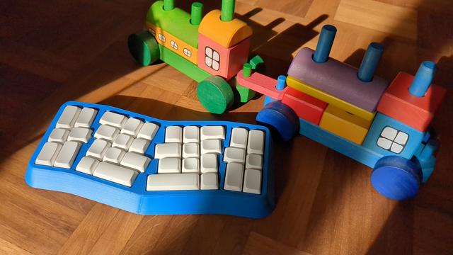 a small keyboard with 34 keys seemingly placed more or less at random in front of a toy train. the keys are white PBS profile blanks, the case is a blue 3d print.