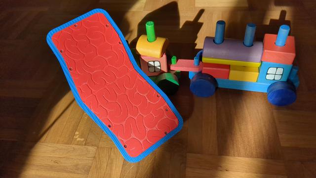 the same keyboard in front of a toy train, flipped to show the bottom. it's an intense red with a brain pattern.
