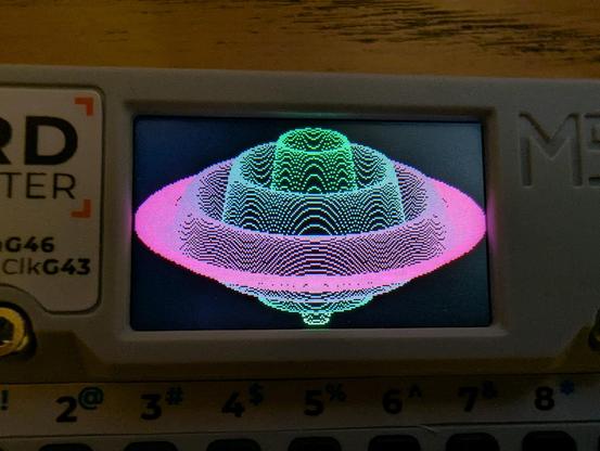 Closeup view of the color display of a card-sized microcontroller device running a graphics program. On a black baground the display shows a 3D line plot of a sinusoidal wave mathematical function with colors ranging from green to pink.