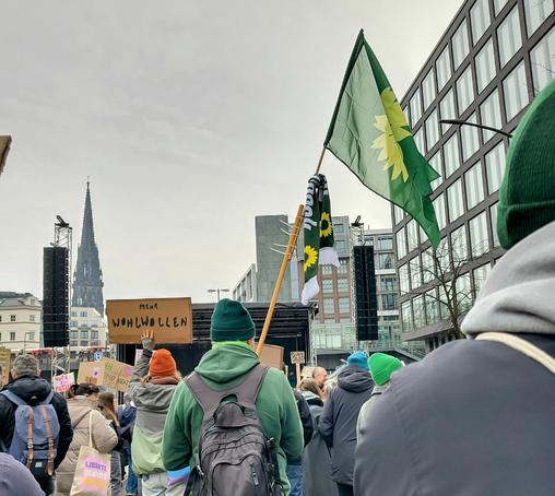 Demonstration in Hamburg mit vielen Menschen. Eine Fahne mit dem Logo von Bündnis 90/Die Grünen.