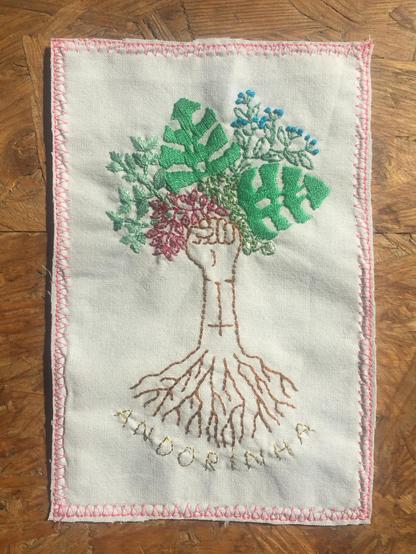 Handmade embroidery representing a trhee with it's roots. The trunc ends on a closed fist, figuring the feminist symbol. The leaves are made of tropical plants and flowers.