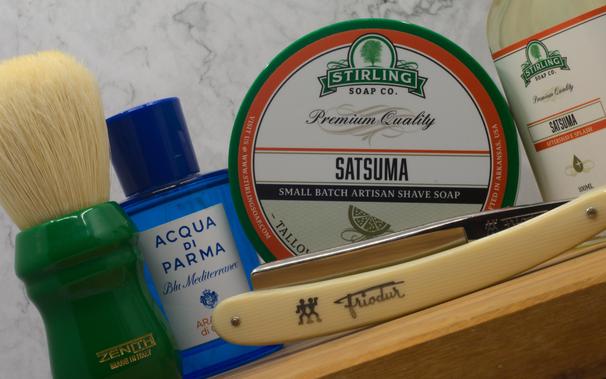 (Le Chat Mistral)
This image shows a collection of men's grooming items arranged on a marble surface. There's a shaving brush with a green resin handle and white bristles on the left. Next to it is a blue bottle of Acqua di Parma Blu Mediterraneo fragrance. In the centre, there's a round container of Stirling Soap Co. Satsuma shaving soap with a green and orange label. To the right, there's a straight razor with off-white scales and a brand name engraved on it. Additionally, there's a bottle of aftershave splash with a similar label to the soap. The items are neatly placed, suggesting a focus on classic shaving tools and high-quality grooming products.