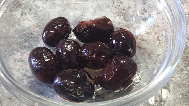 Foto de unas olivas negras aliñadas en un bol transparente sobre una encimera de cocina.
Brillan y se nota que están blanditas. Y se aprecian algunos de los cortes efectuados en el proceso.