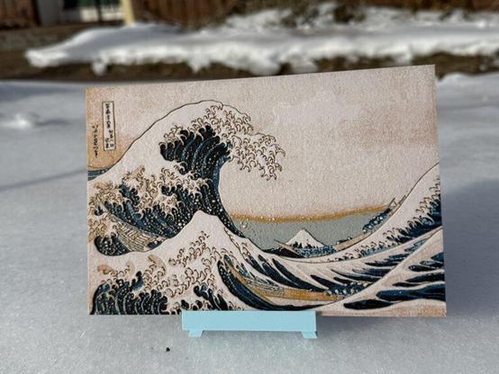A 3D printed reproduction of Hokusai's "Great Wave Off of Kanagawa", on a blue 3D printed easel, sitting on the snowy front lawn of my house.