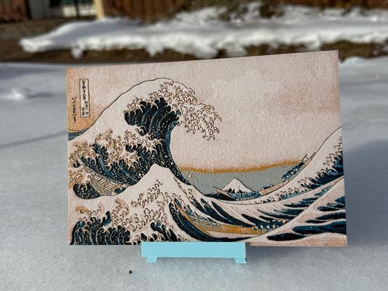 A 3D printed reproduction of Hokusai's "Great Wave Off of Kanagawa", on a blue 3D printed easel, sitting on the snowy front lawn of my house.